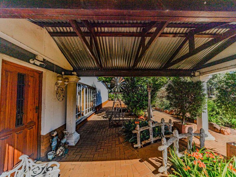 A covered patio area featuring brick paving, timber support beams, and a corrugated metal roof, providing a shaded outdoor space.