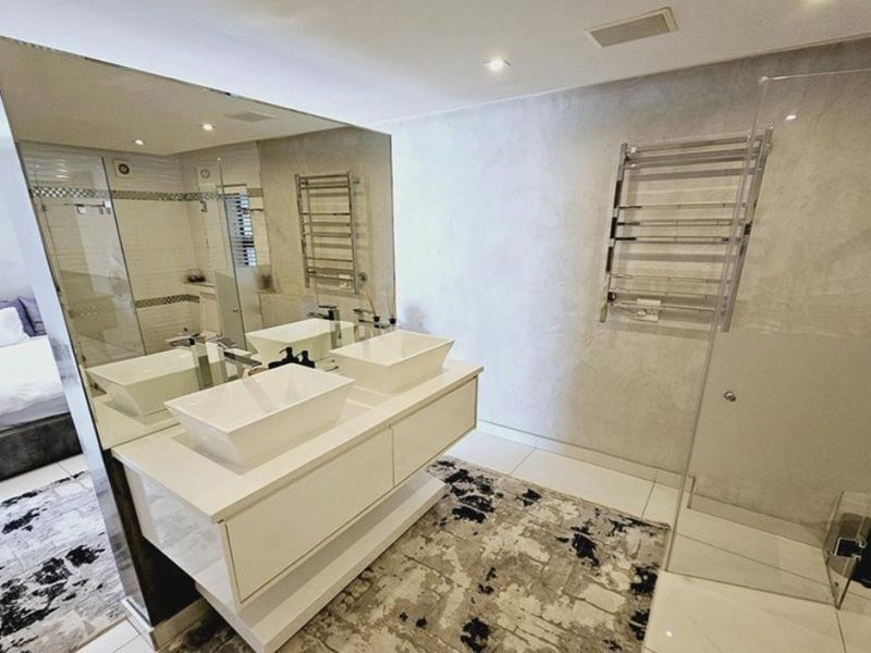 Modern bathroom featuring a double vanity with vessel sinks, a large wall mirror, a heated towel rail, and a glass-enclosed shower.