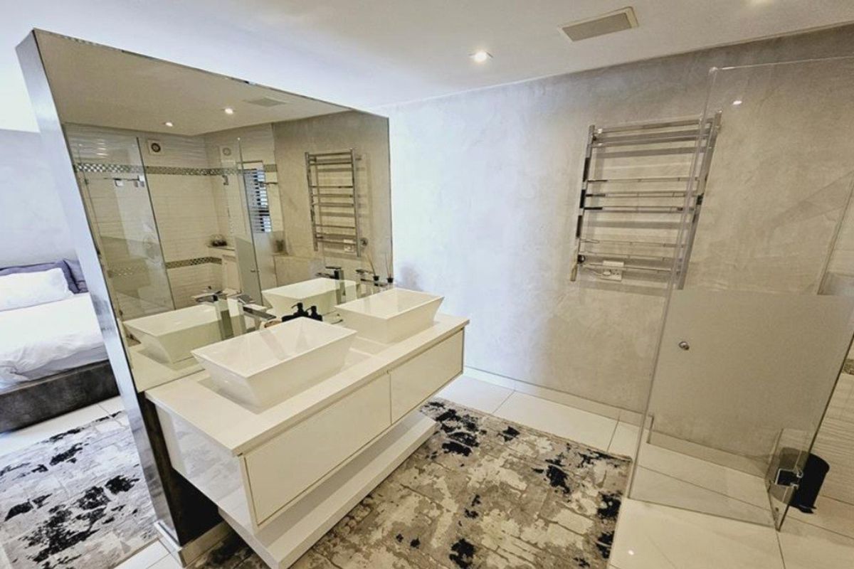 Modern bathroom featuring a double vanity with vessel sinks, a large wall mirror, a heated towel rail, and a glass-enclosed shower.