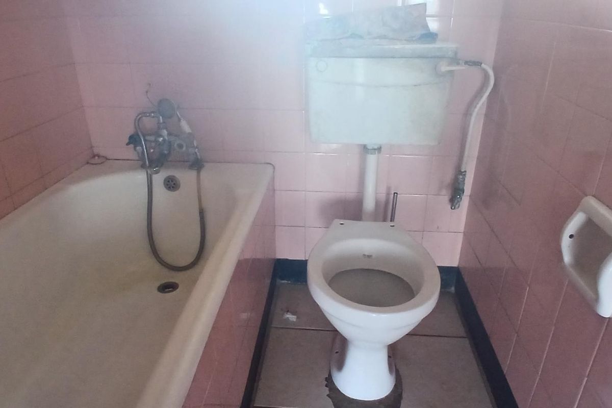 A dated bathroom featuring original pink wall tiles, a standard bathtub, and a toilet. The space requires modernization of fixtures and finishes.