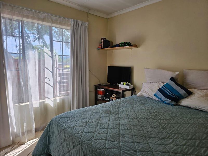 A functional bedroom featuring a large window with natural light, neutral wall tones, and classic coving detail.