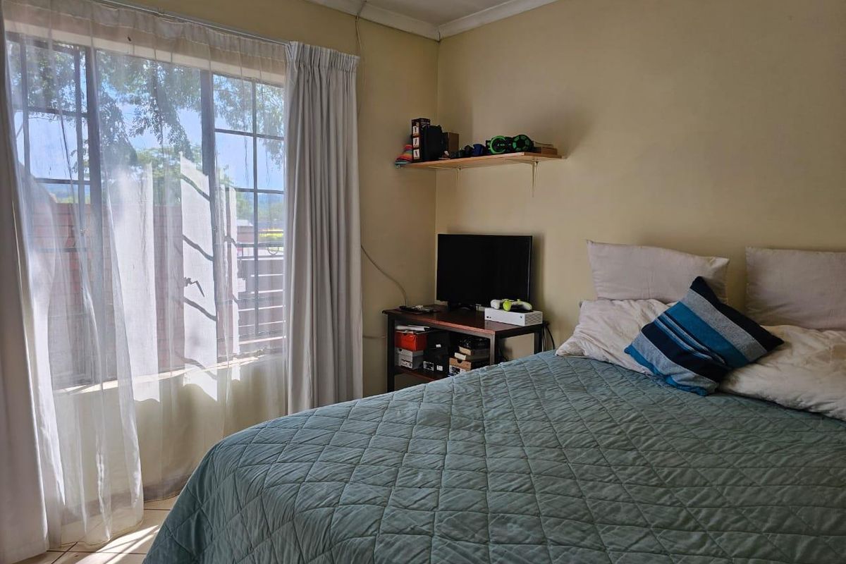 A functional bedroom featuring a large window with natural light, neutral wall tones, and classic coving detail.