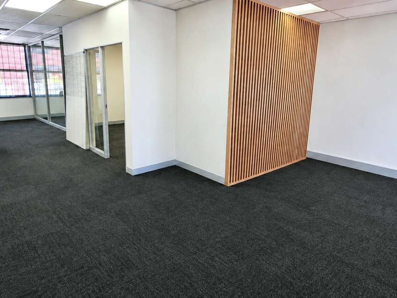 A modern, open-plan office space featuring dark carpeting, a decorative timber slat feature wall, and glass-partitioned meeting areas with recessed ceiling lighting.