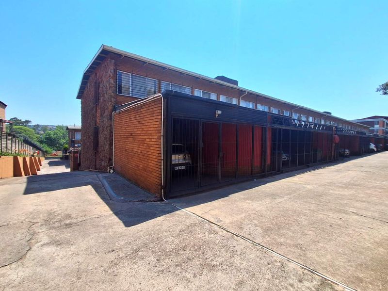 Exterior view of a townhouse complex featuring a row of secure, gated garages with brick and stone facade construction and a concrete driveway.