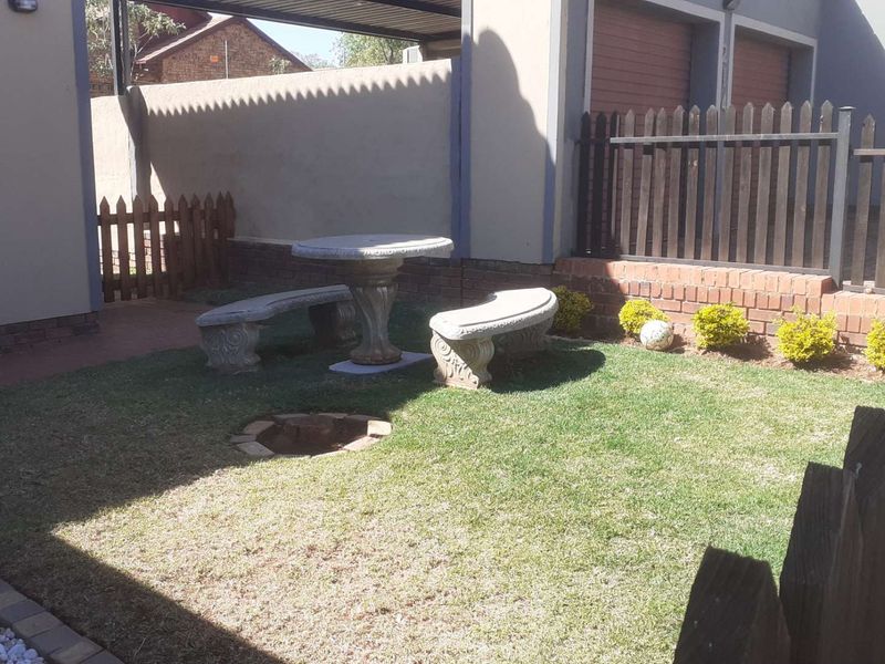 A rear garden area featuring a small lawn, brick boundary walls, and a picket fence, adjacent to the property's garage and driveway.