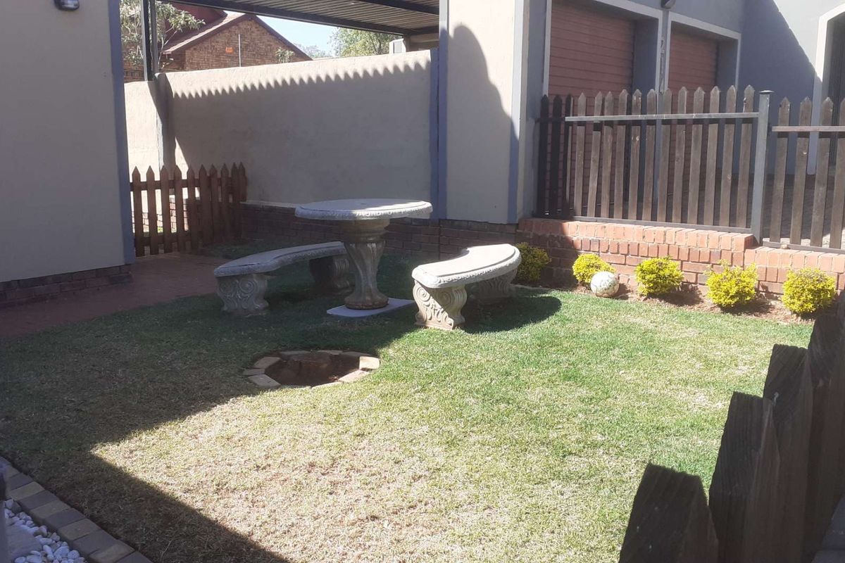 A rear garden area featuring a small lawn, brick boundary walls, and a picket fence, adjacent to the property's garage and driveway.