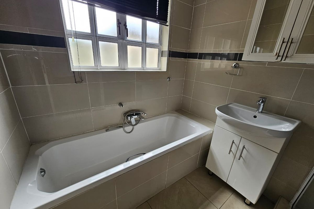 A functional bathroom featuring a built-in bathtub, a wall-mounted vanity with a basin, and tiled walls with a decorative border.