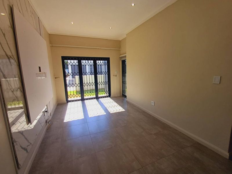 A bright, empty living room featuring large format floor tiles, recessed lighting, and a secure sliding glass door leading to the exterior.