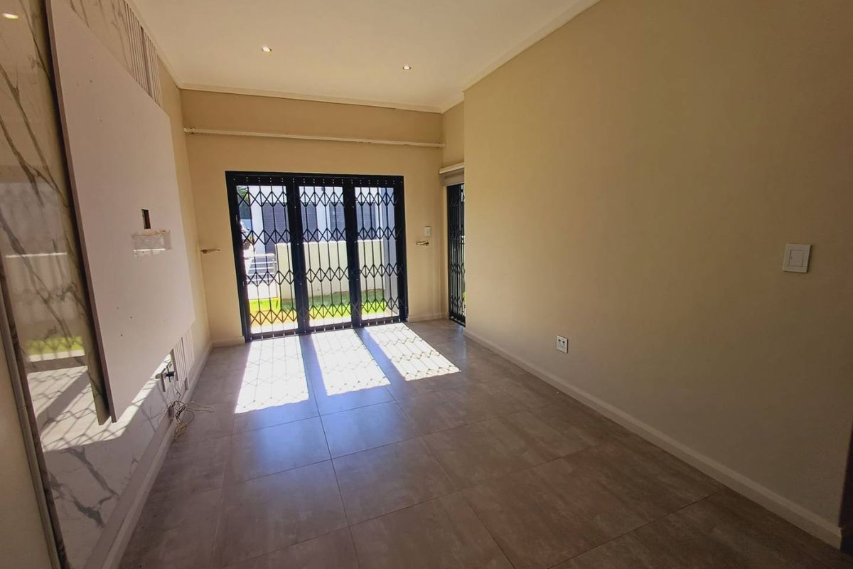 A bright, empty living room featuring large format floor tiles, recessed lighting, and a secure sliding glass door leading to the exterior.