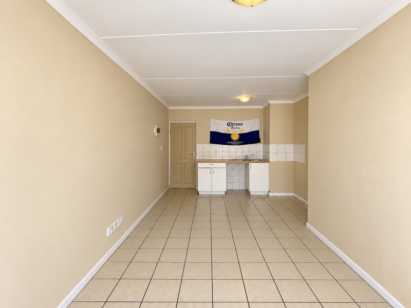 An empty kitchen area featuring tiled flooring, basic cabinetry with a sink, and a tiled backsplash, offering a blank canvas for renovation.