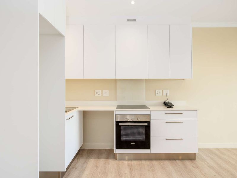 Modern kitchen featuring clean white cabinetry, integrated electric hob and oven, glass splashback, and light wood-look laminate flooring.