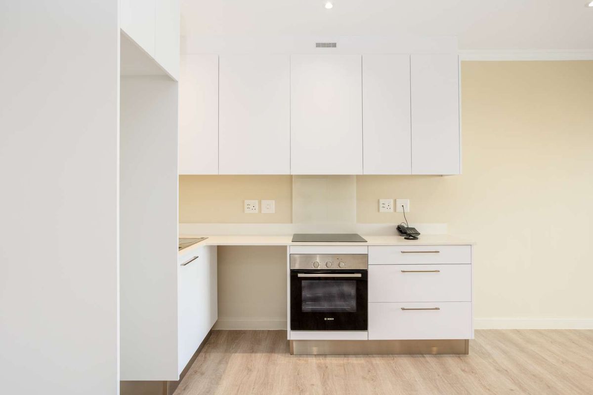 Modern kitchen featuring clean white cabinetry, integrated electric hob and oven, glass splashback, and light wood-look laminate flooring.