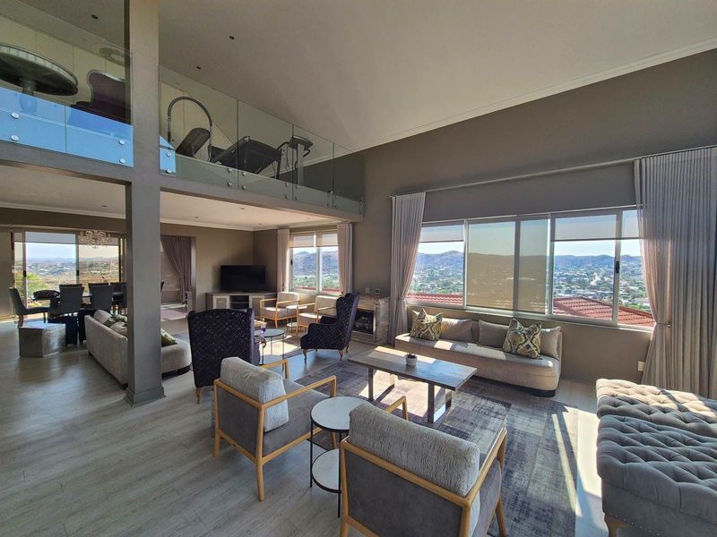 Spacious open-plan living area featuring a mezzanine level with glass balustrade, large windows offering panoramic views, and modern laminate flooring.