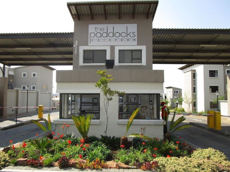 The secure entrance gatehouse of The Paddocks complex, featuring a boom gate system and well-maintained landscaped gardens.