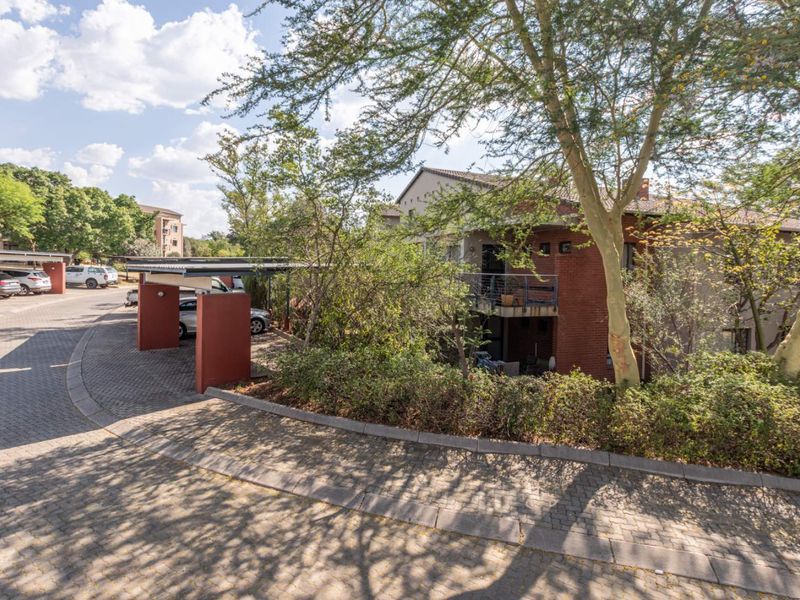 Exterior view of the apartment complex featuring a paved driveway, covered carport parking, and brick building facade with balcony access.