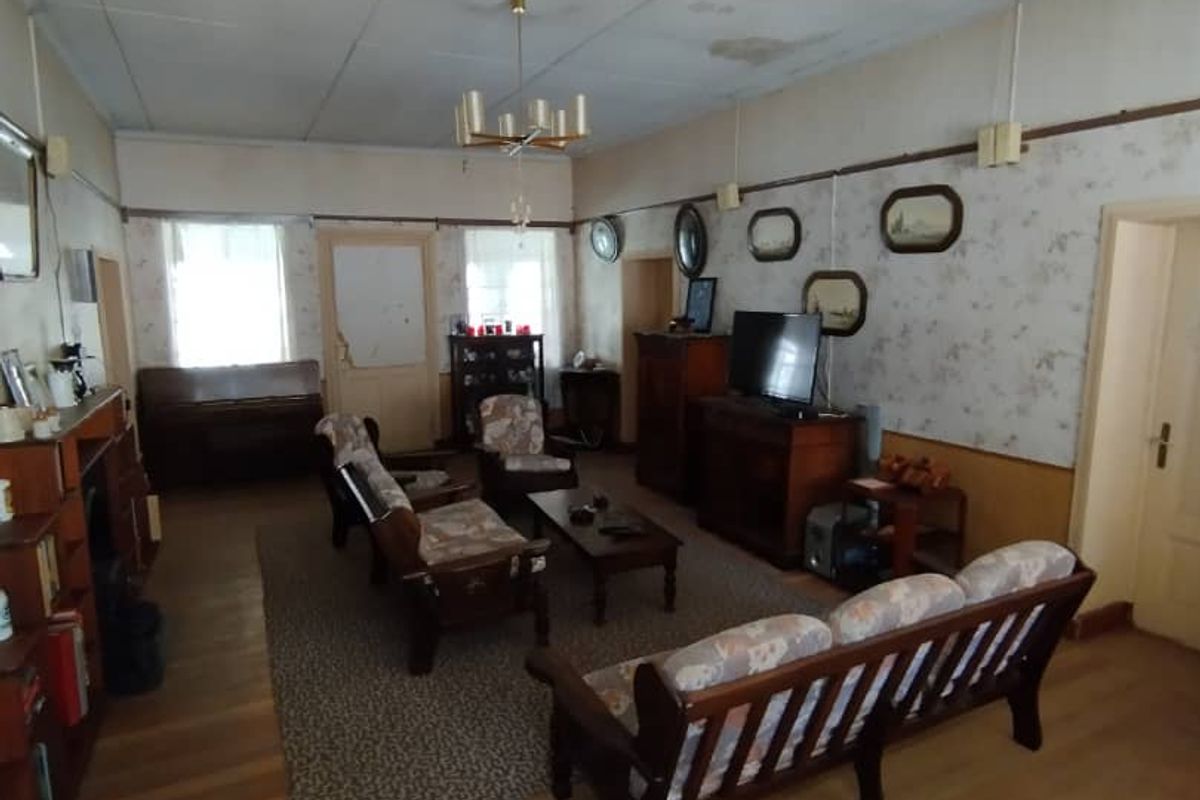 Spacious living room featuring original timber flooring, traditional wallpaper, and a drop ceiling, offering a classic layout with potential for modernization.