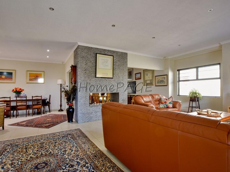 Spacious open-plan living and dining area featuring a central stone-clad fireplace, tiled flooring, and recessed lighting throughout.