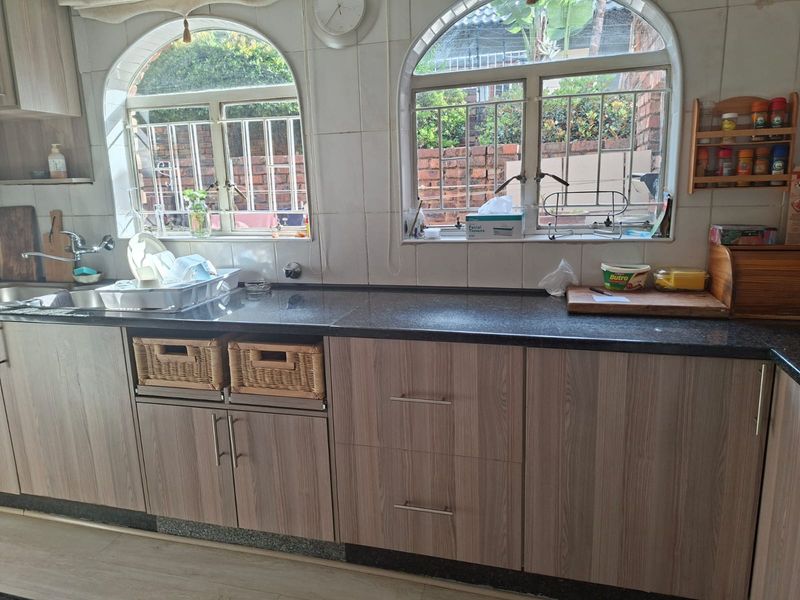 A functional kitchen featuring granite countertops, wood-look laminate cabinetry, and dual arched windows with security bars, providing ample natural light and workspace.