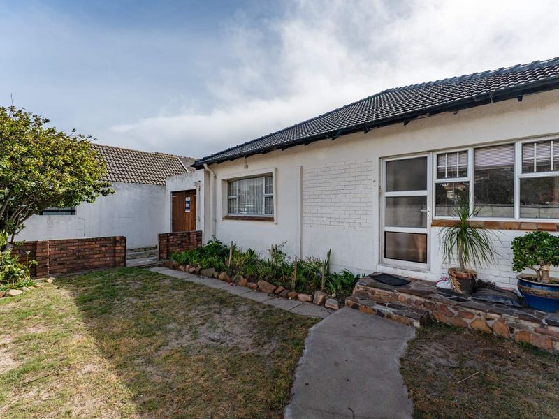 Rear exterior view of the house featuring a tiled roof, white painted brick facade, and a small garden area with a concrete pathway.