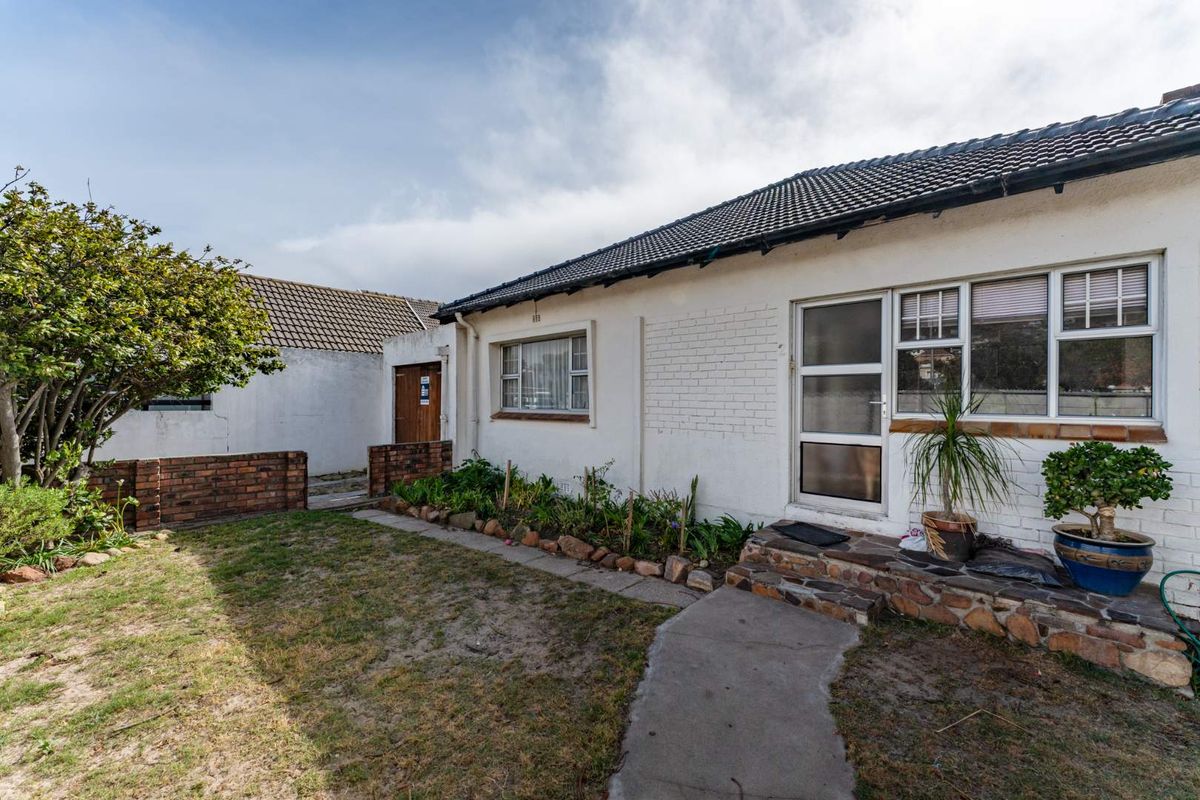 Rear exterior view of the house featuring a tiled roof, white painted brick facade, and a small garden area with a concrete pathway.