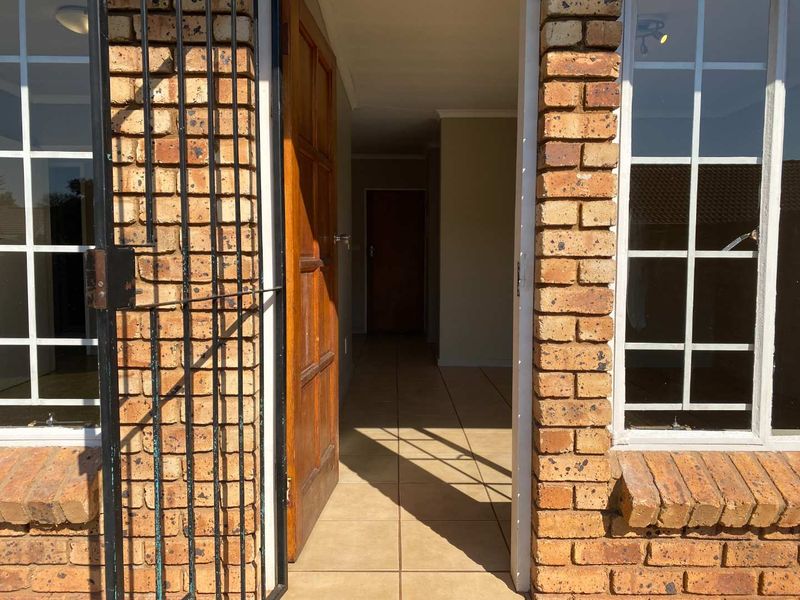 Entrance view of a townhouse featuring a brick facade, security gate, and tiled flooring leading into the interior hallway.
