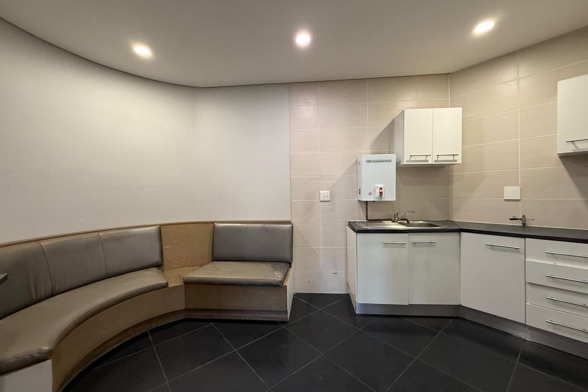 A functional office kitchenette area featuring built-in cabinetry, a stainless steel sink, tiled splashbacks, and integrated curved bench seating.