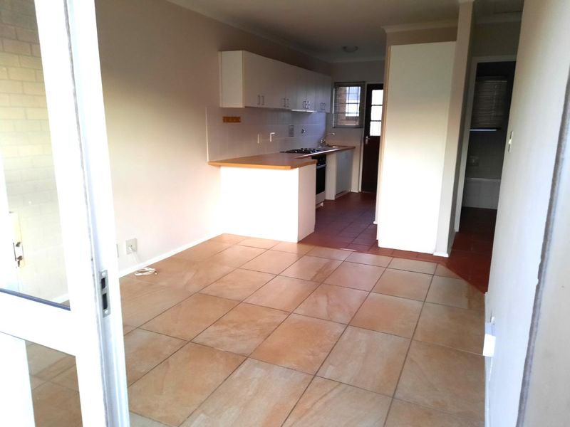 An open-plan kitchen featuring tiled flooring, built-in cabinetry with laminate countertops, and integrated cooking appliances, presented in a clean, vacant state.
