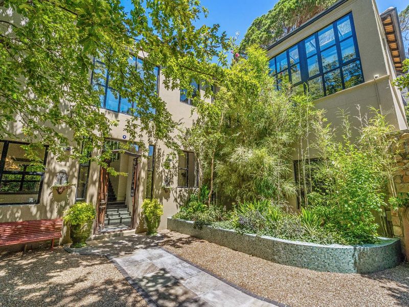 A beautifully landscaped courtyard entrance featuring a stone pathway, mosaic-tiled planter bed, and large multi-pane windows on a two-story exterior facade.