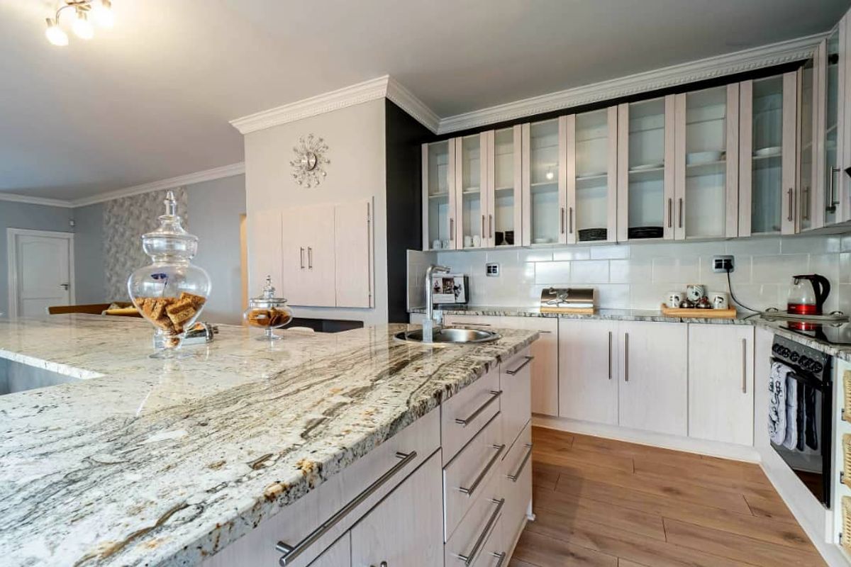Modern kitchen featuring granite countertops, light wood cabinetry with glass-fronted upper units, subway tile backsplash, and integrated oven.