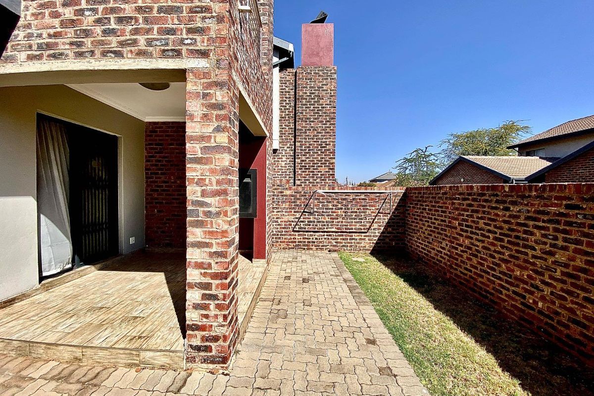 A private rear courtyard featuring a covered patio with tiled flooring, brick boundary walls, and a paved walkway alongside a small lawn area.