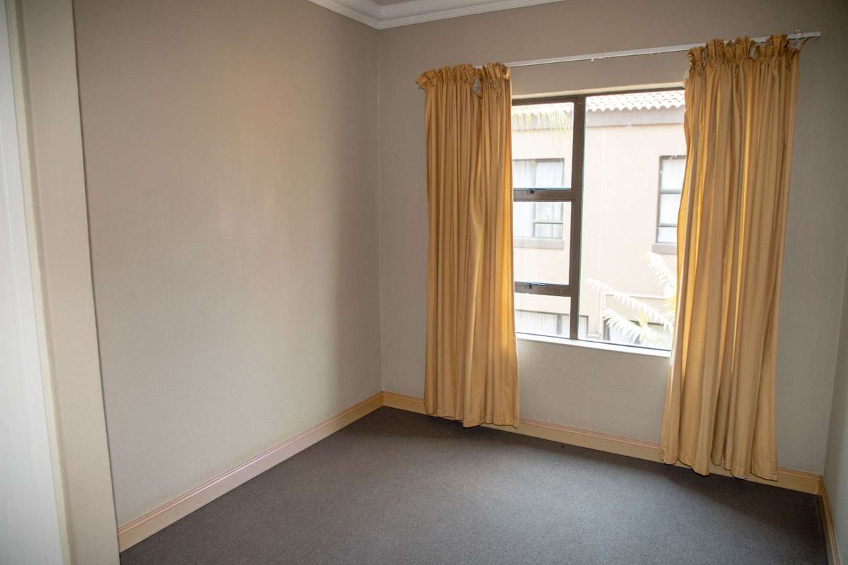 A neutral-toned bedroom featuring carpeted flooring, a window with natural light, and simple crown molding.