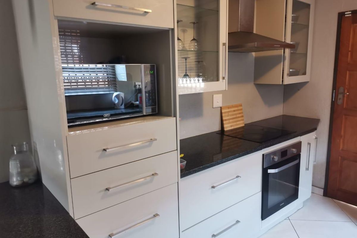 Modern kitchen featuring sleek white cabinetry, dark granite countertops, a built-in oven, glass-top hob, and stainless steel extractor fan.