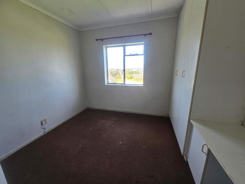 An empty bedroom featuring built-in cupboards, carpeted flooring, and a window with an exterior view.