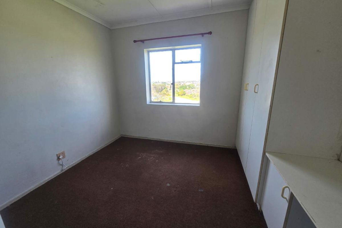 An empty bedroom featuring built-in cupboards, carpeted flooring, and a window with an exterior view.