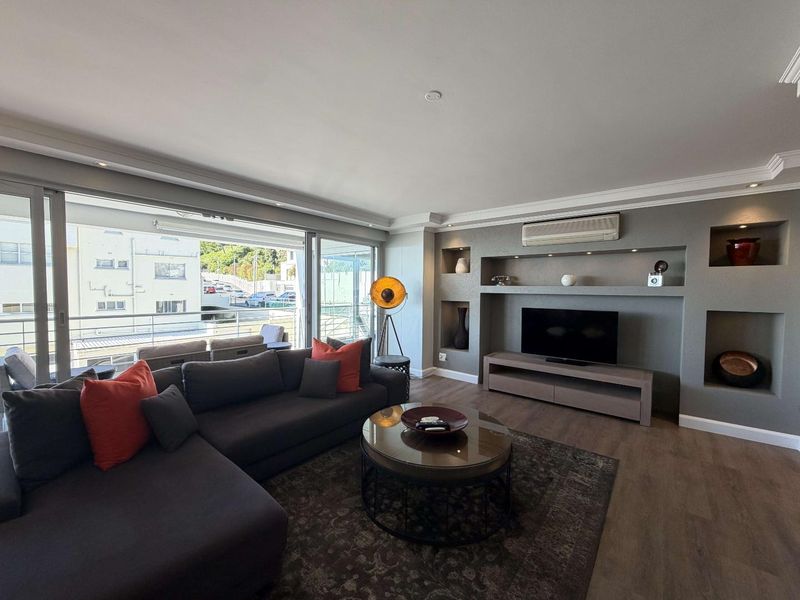 Modern living room featuring a custom built-in media wall with recessed shelving, air conditioning, and large sliding doors leading to an outdoor balcony.