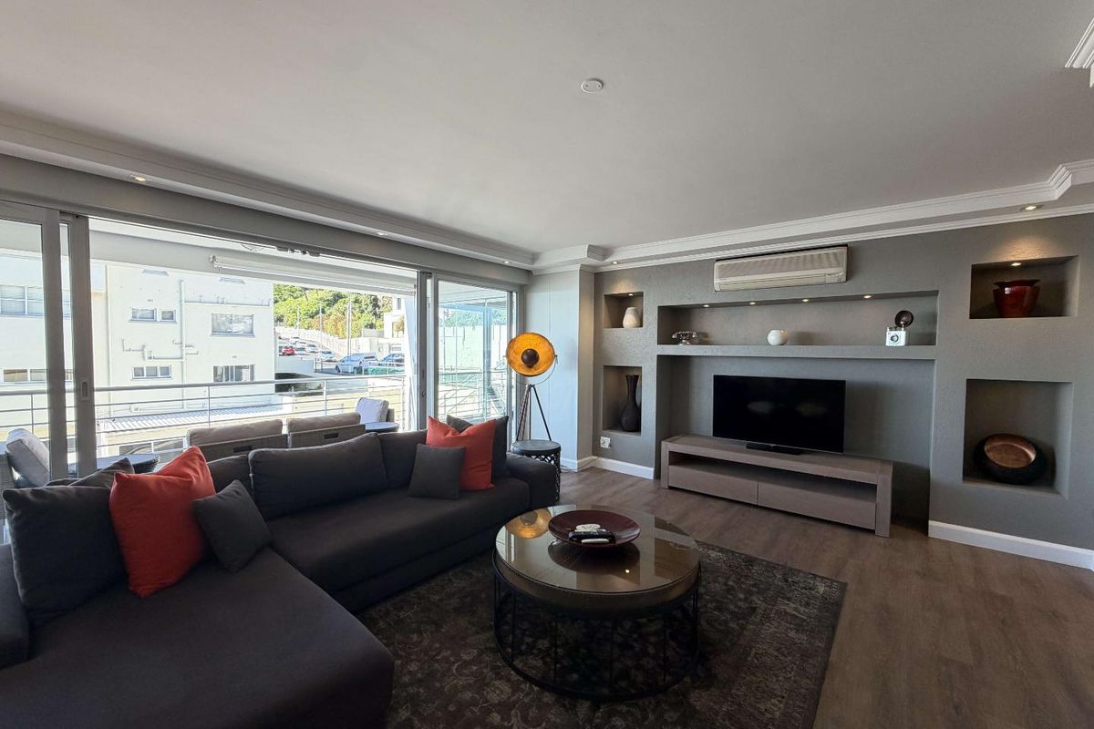 Modern living room featuring a custom built-in media wall with recessed shelving, air conditioning, and large sliding doors leading to an outdoor balcony.