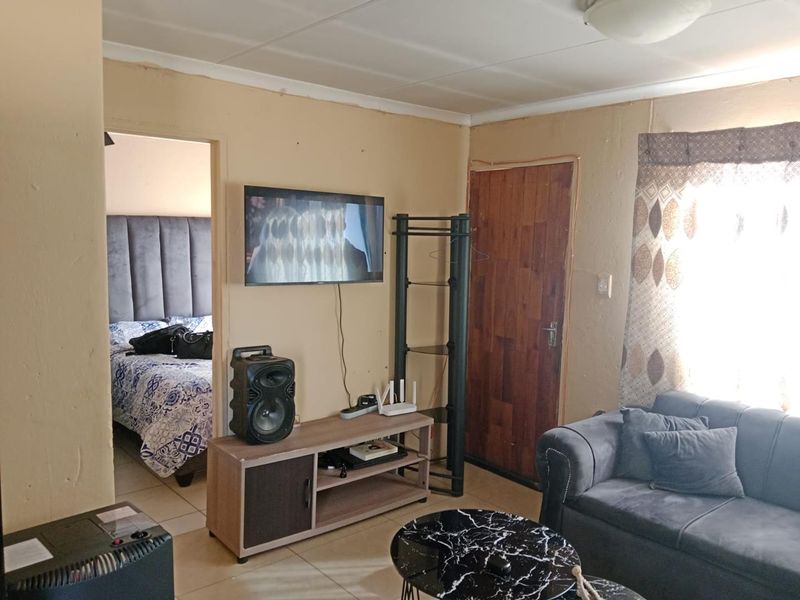 A living room area featuring tiled flooring and a timber door, with visible wear on the wall surfaces.