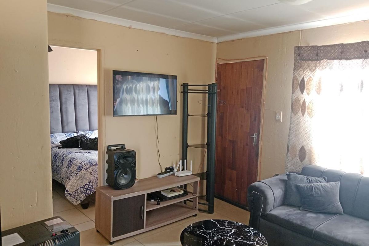 A living room area featuring tiled flooring and a timber door, with visible wear on the wall surfaces.