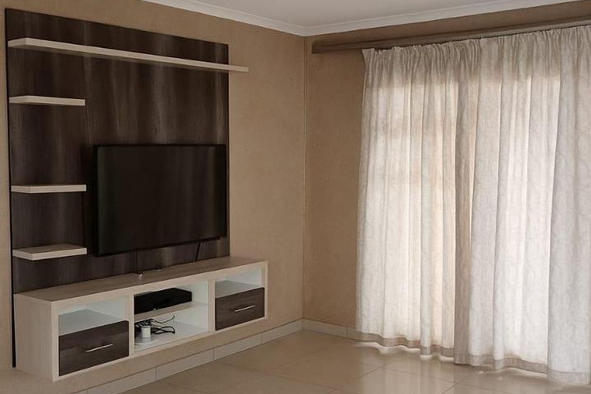 A bright and spacious living room featuring neutral tiled flooring, a modern built-in media unit, and large windows with installed curtain tracks.