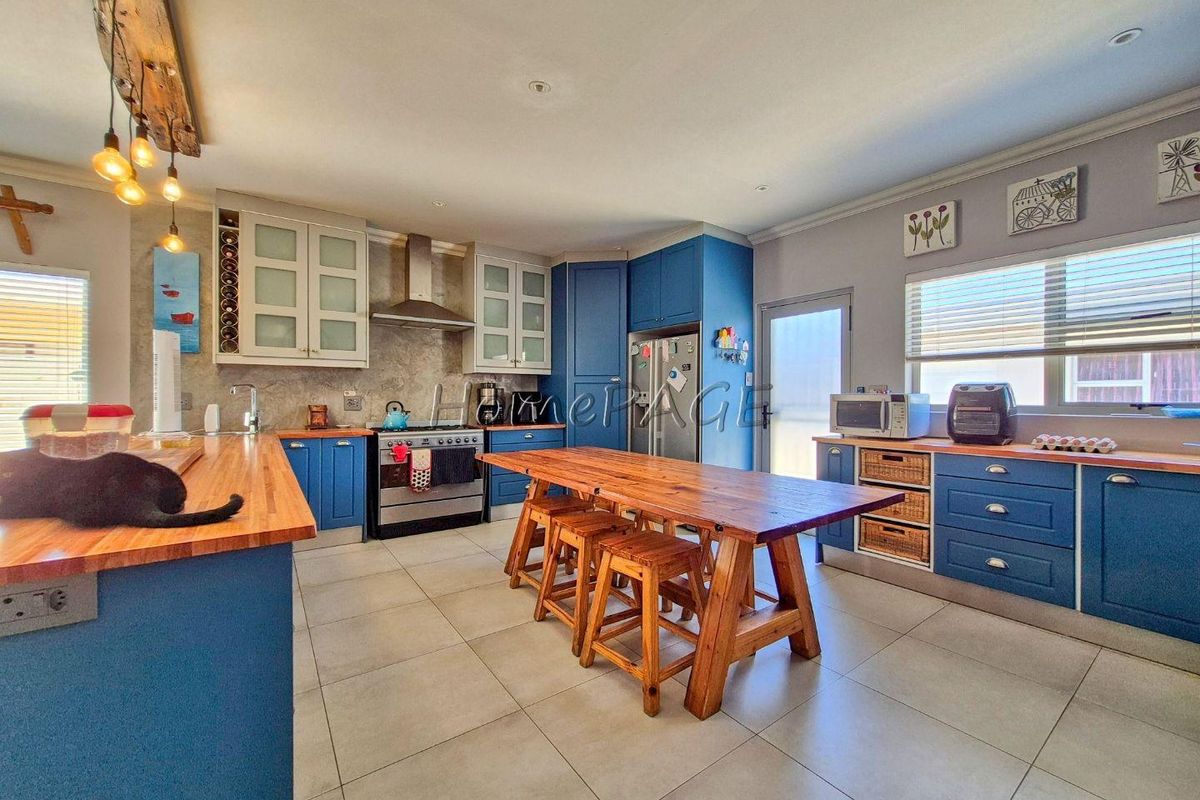 A spacious kitchen featuring blue cabinetry, wooden countertops, a stainless steel extractor fan, and tiled flooring with a central wooden island.