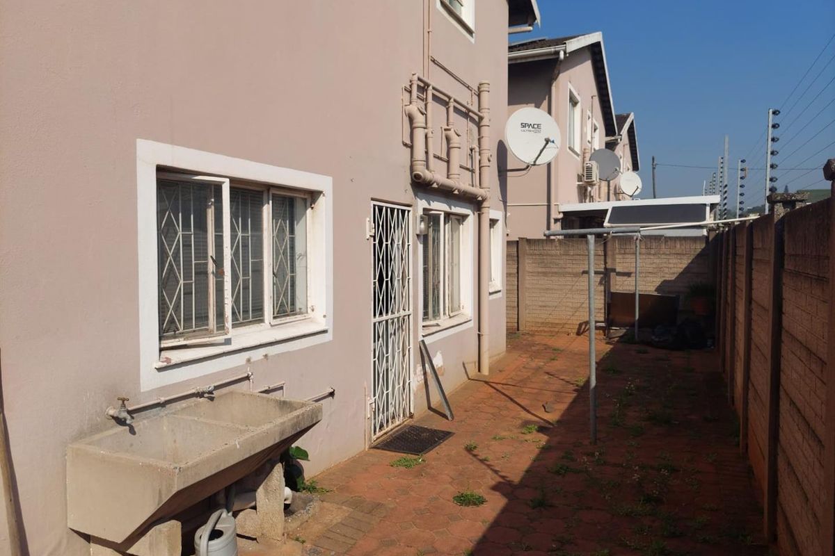 Rear exterior view of the townhouse featuring a paved courtyard, concrete wash trough, and security features on windows and doors.