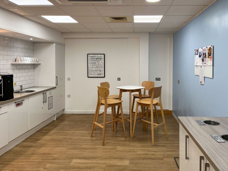 A modern office kitchenette featuring white cabinetry, a subway tile backsplash, stainless steel sink, and durable laminate flooring with integrated waste disposal.
