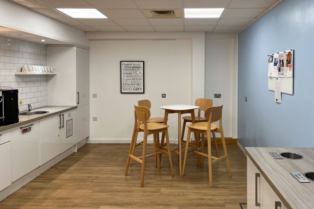A modern office kitchenette featuring white cabinetry, a subway tile backsplash, stainless steel sink, and durable laminate flooring with integrated waste disposal.