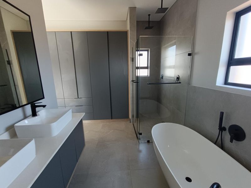 Modern bathroom featuring a double vanity, freestanding bathtub, walk-in shower with rain head, and ample built-in storage cabinetry with a contemporary finish.