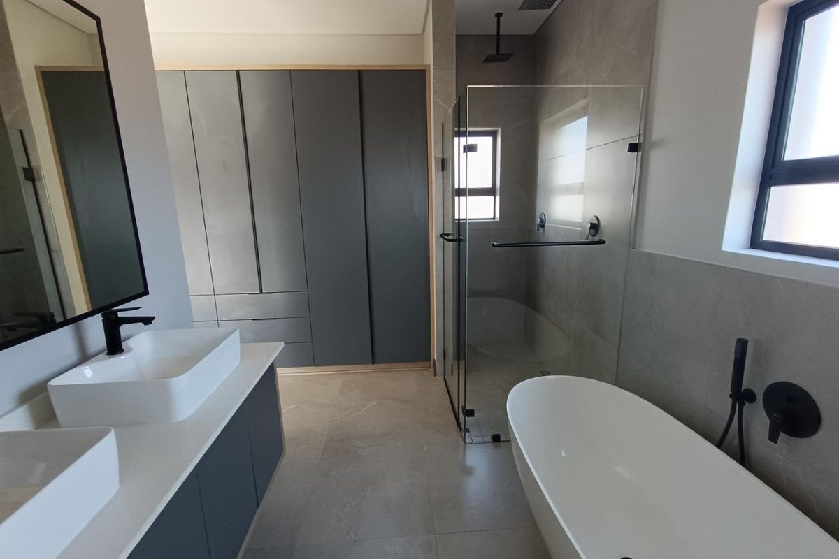 Modern bathroom featuring a double vanity, freestanding bathtub, walk-in shower with rain head, and ample built-in storage cabinetry with a contemporary finish.