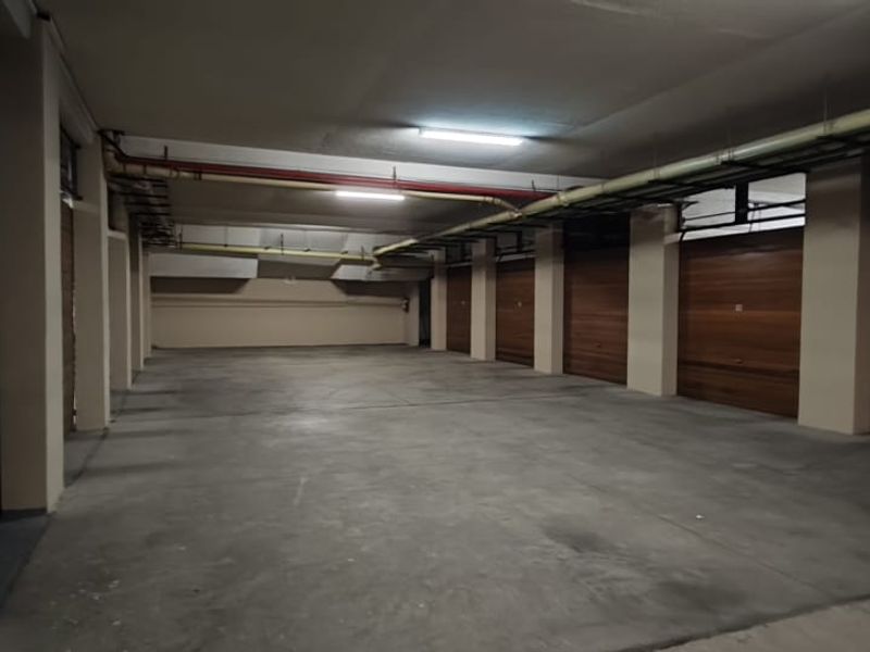 A spacious, well-lit underground parking garage featuring multiple individual garage bays with wooden-finish doors and concrete flooring.