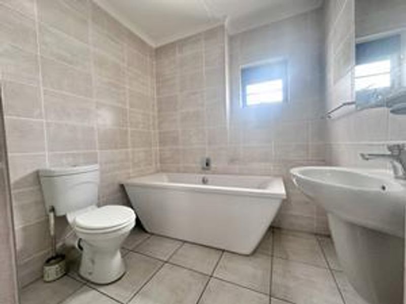 A clean, modern bathroom featuring a freestanding bathtub, pedestal basin, and toilet with neutral floor-to-ceiling wall tiling.