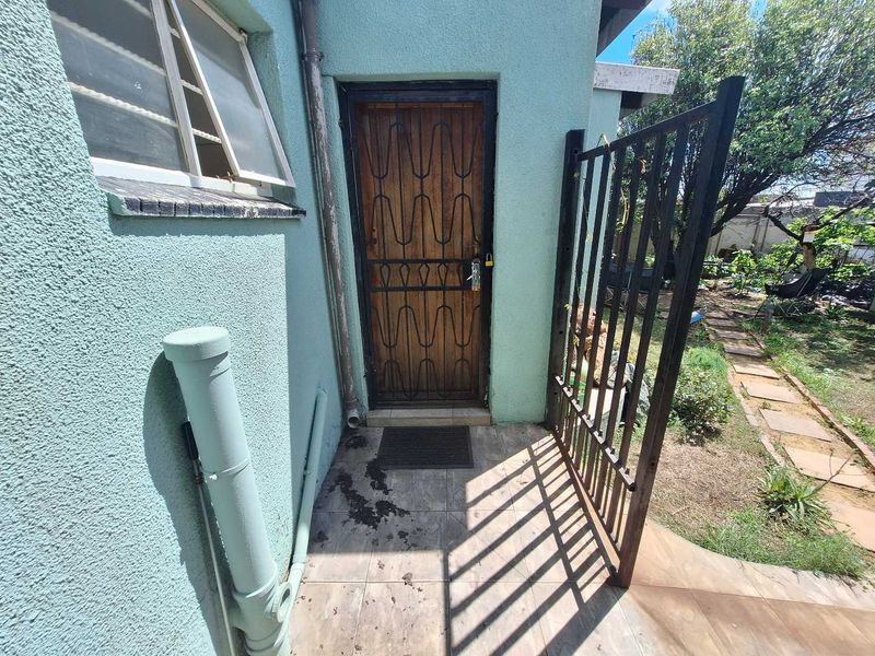 Rear exterior view showing a security gate, tiled patio area, and access to the garden with a paved pathway.