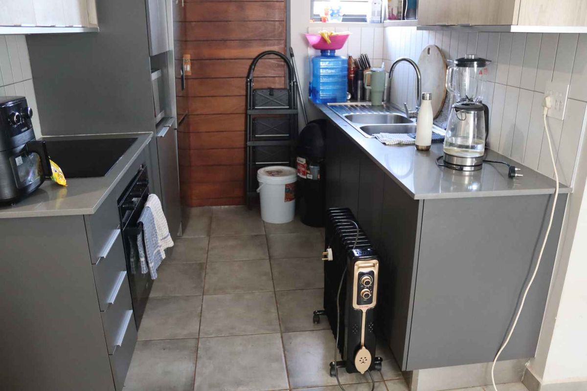 A compact kitchen featuring modern grey cabinetry, stone-look countertops, a double stainless steel sink, and a built-in oven with a hob.