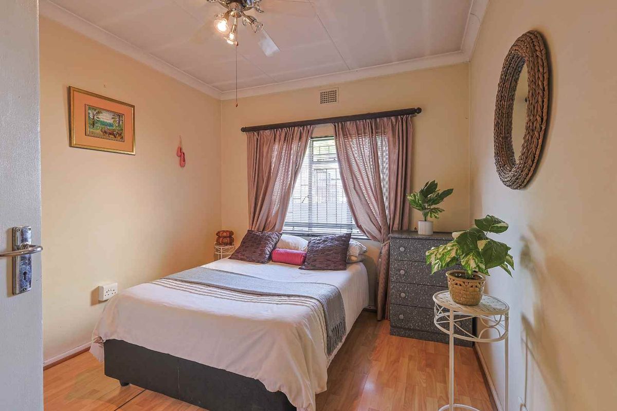 A compact bedroom featuring laminate flooring, a ceiling fan, and a window with curtain tracks.
